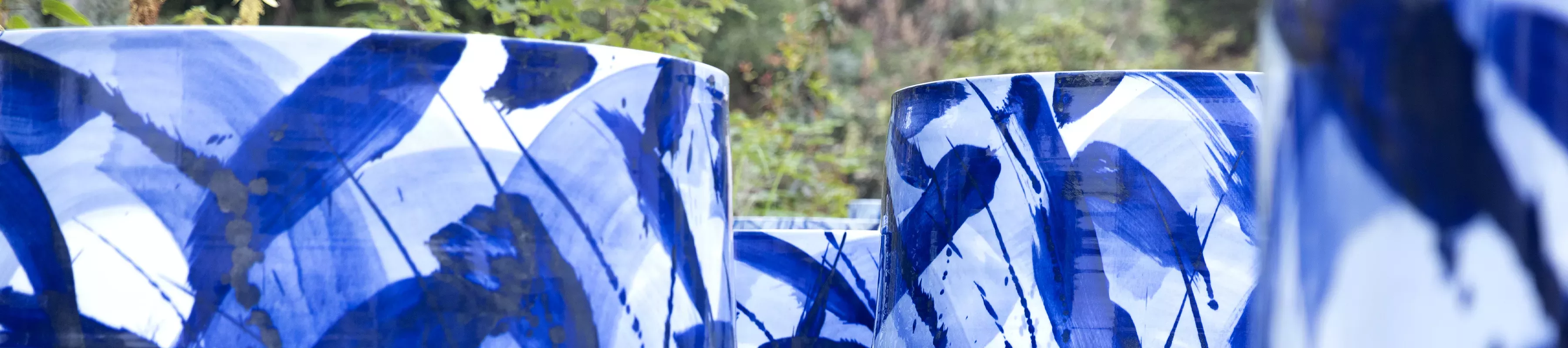 Expressions in Blue by Felicity Aylieff The tops of monumental porcelain pots glazed in blue and white patterns with a glimpse of trees in the background.