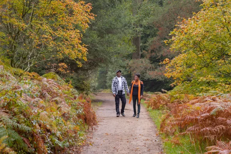 Horsebridge Wood at Wakehurst, James Ratchford © RBG Kew A black couple walking down a pathway through beautiful autumn trees