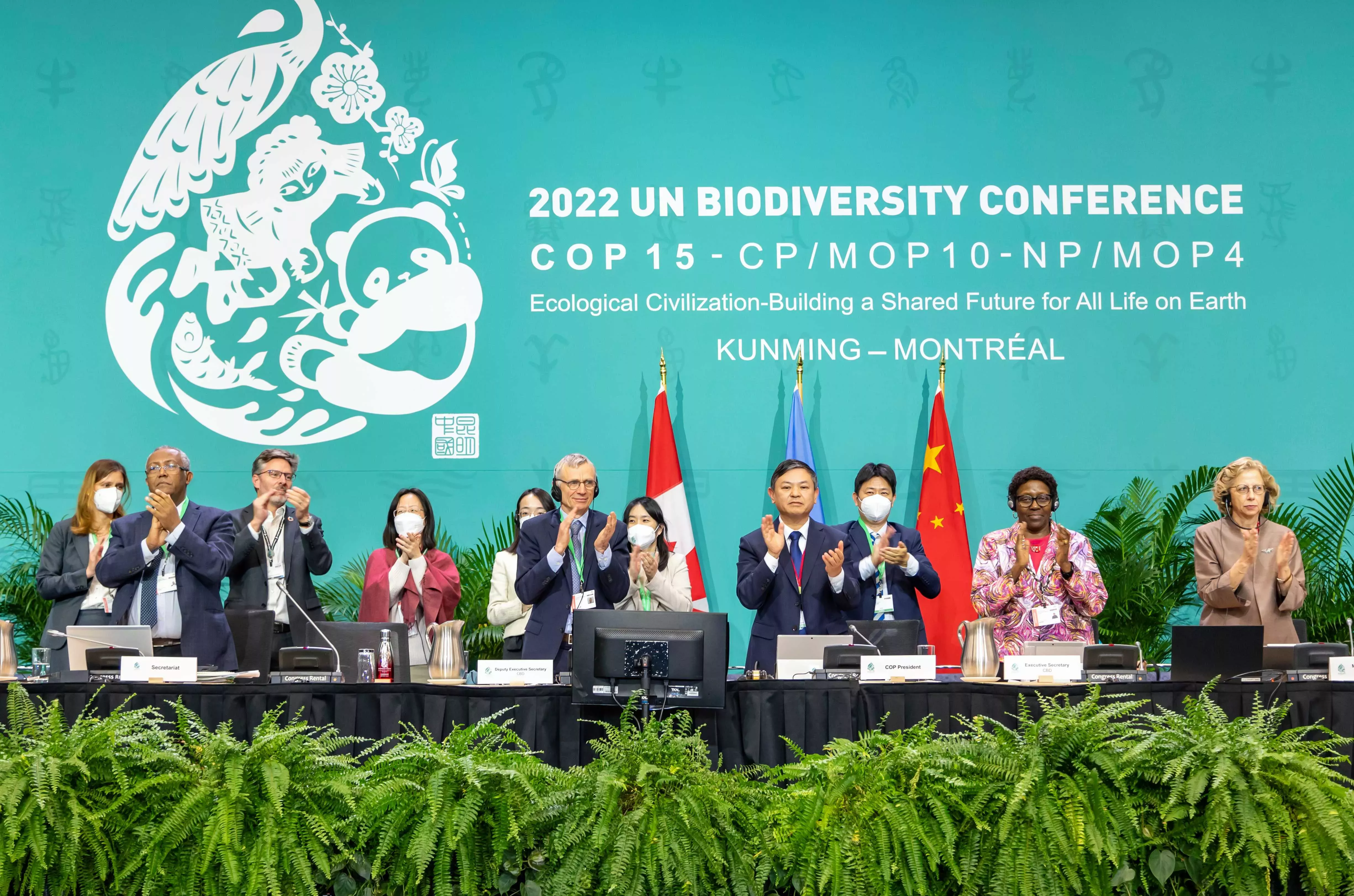 Delegates standing and applauding in front of a blue background for COP15 and the flags of Canada and China