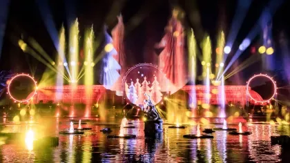 The Palm House at Kew Gardens lit up with fountains and red and orange lights, with christmas trees projected through a giant circle