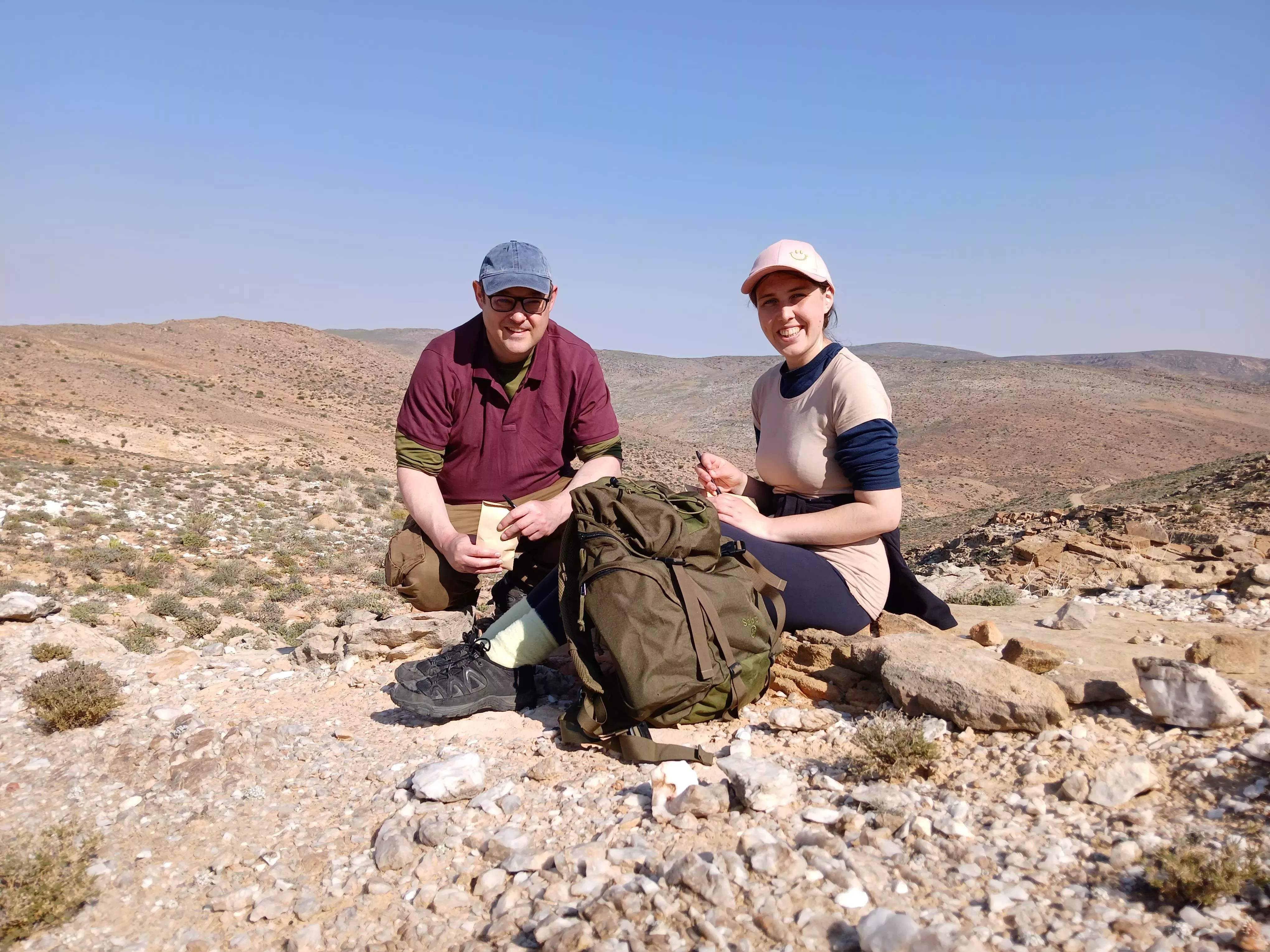 Scientists David Whitehead and Chloe Pate doing fieldwork in South Africa, June 2024 Two scientists sitting on the desert floor with research materials