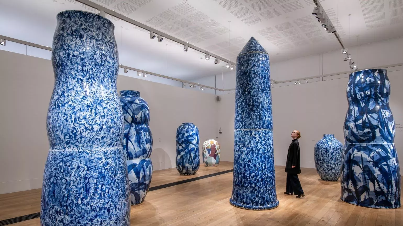 A woman looking up at a huge ceramic pot, in a room filled with monumental porcelain pieces.