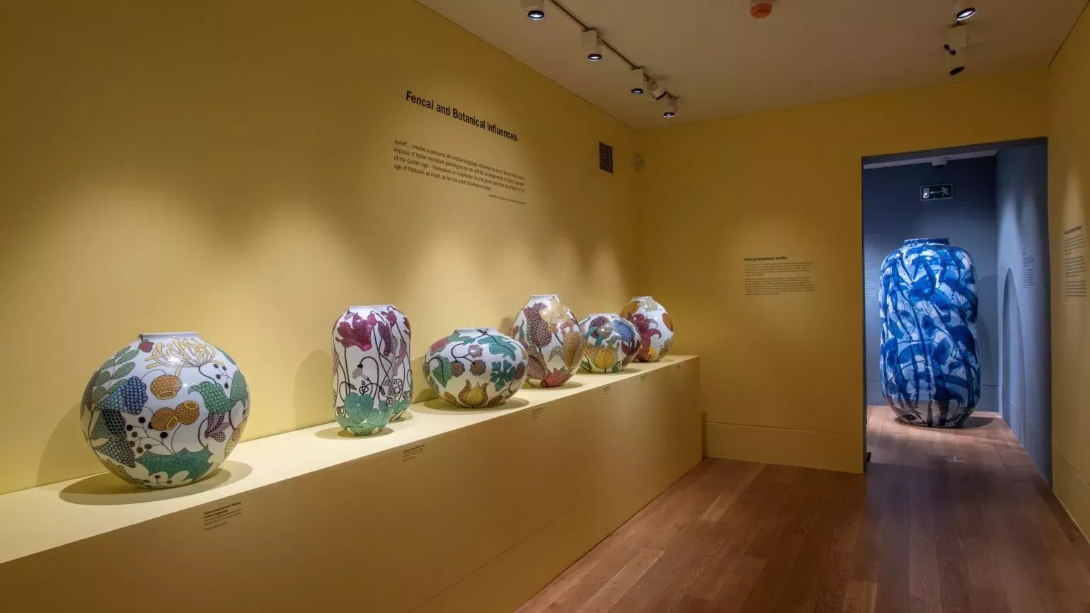 A yellow room filled with colourful pots, with a glimpse into the next room.