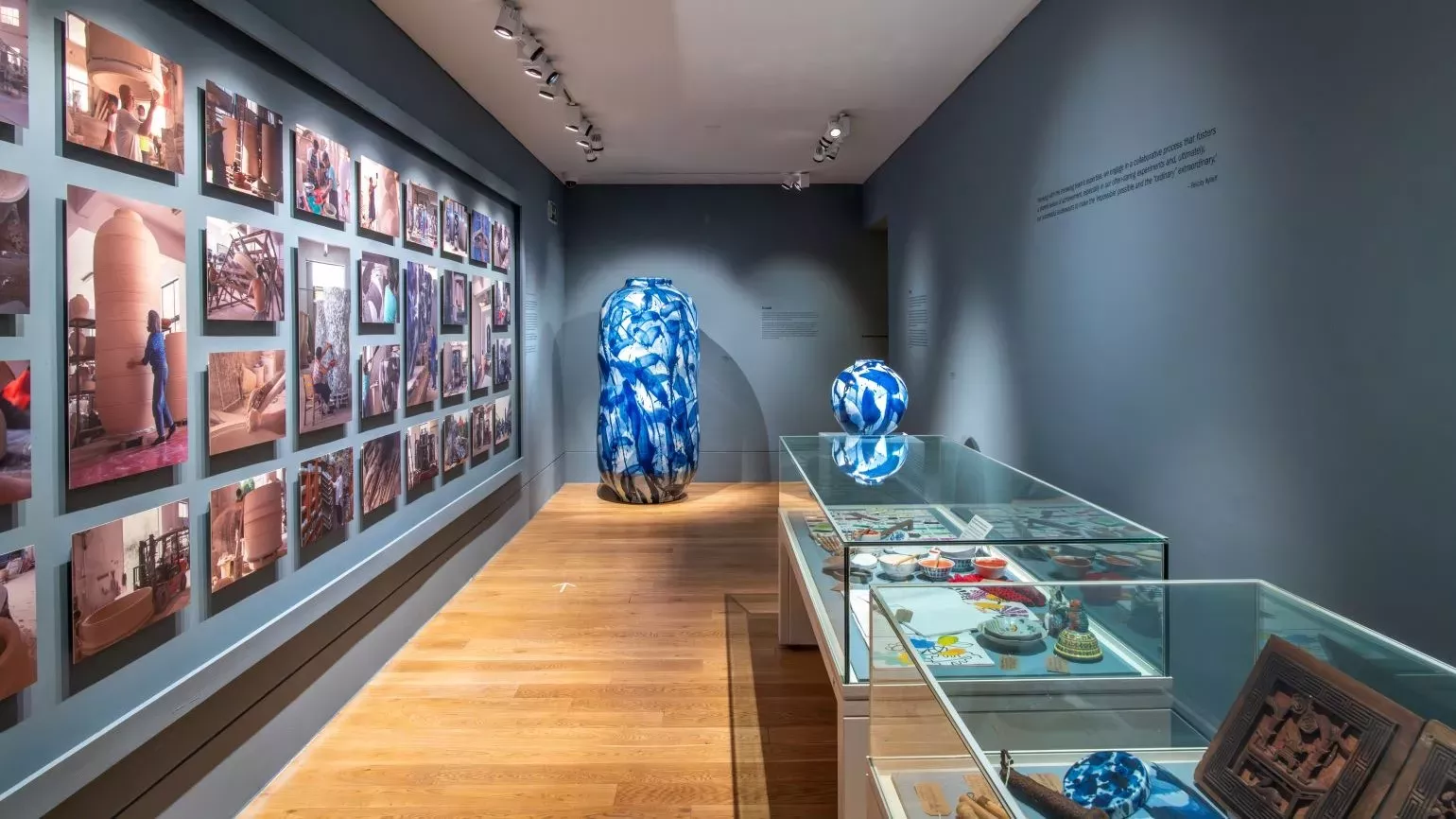 Two large pots at the end of a gallery room, with a wall filled with photographs on the left and display cases on the right.
