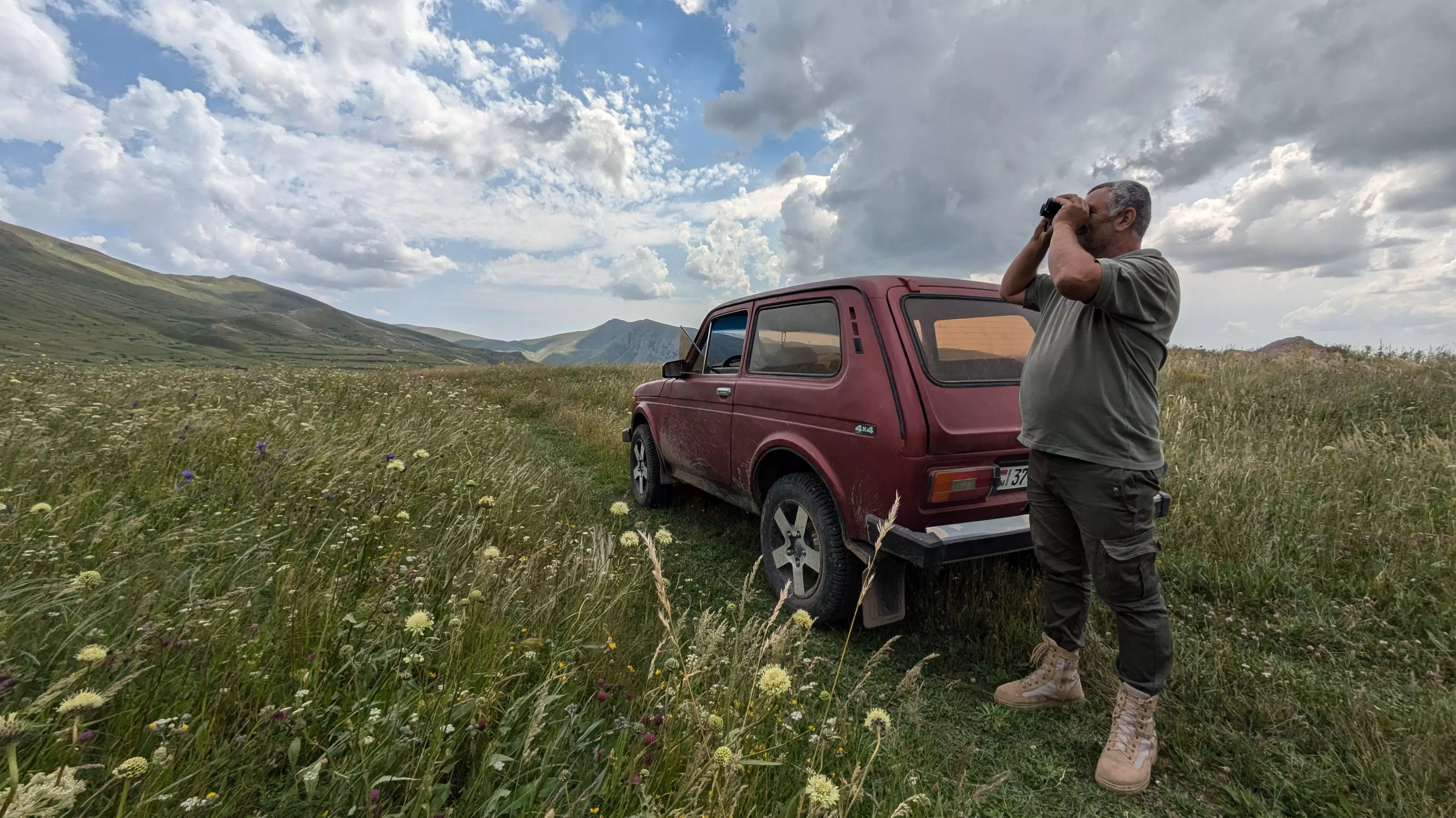 Local rangers hold vast knowledge of these ecosystems, Lydia Shellien-Walker © RBG Kew A person stood next to a car surveying the area with binoculars in a wide valley filled with meadow flowers