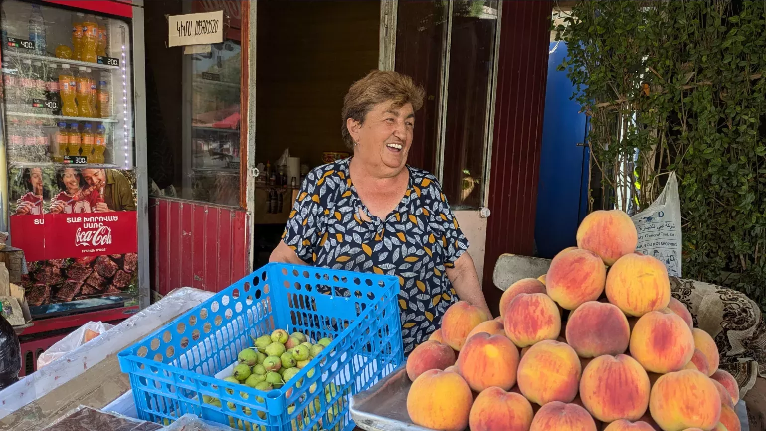 Kima shows the team her fresh fruit and home made products on her market stall, Lydia Shellien-Walker © RBG Kew A person smiling at a food market stall with a pyramid of fruit