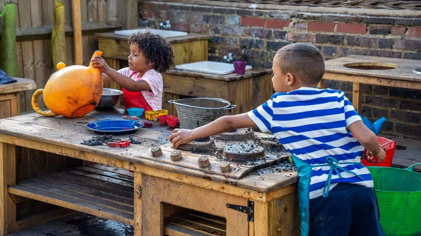 Mud Kitchen at Wakehurst, Visual Air © RBG Kew A young boy leans over a wooden oven, whilst a girl holds up a plastic watering can.