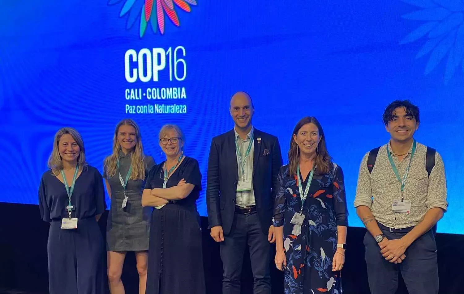Kew representatives at COP16 in Cali, Colombia, Maria Mira © RBG Kew Six people smiling in front of a blue background that says 'COP16'