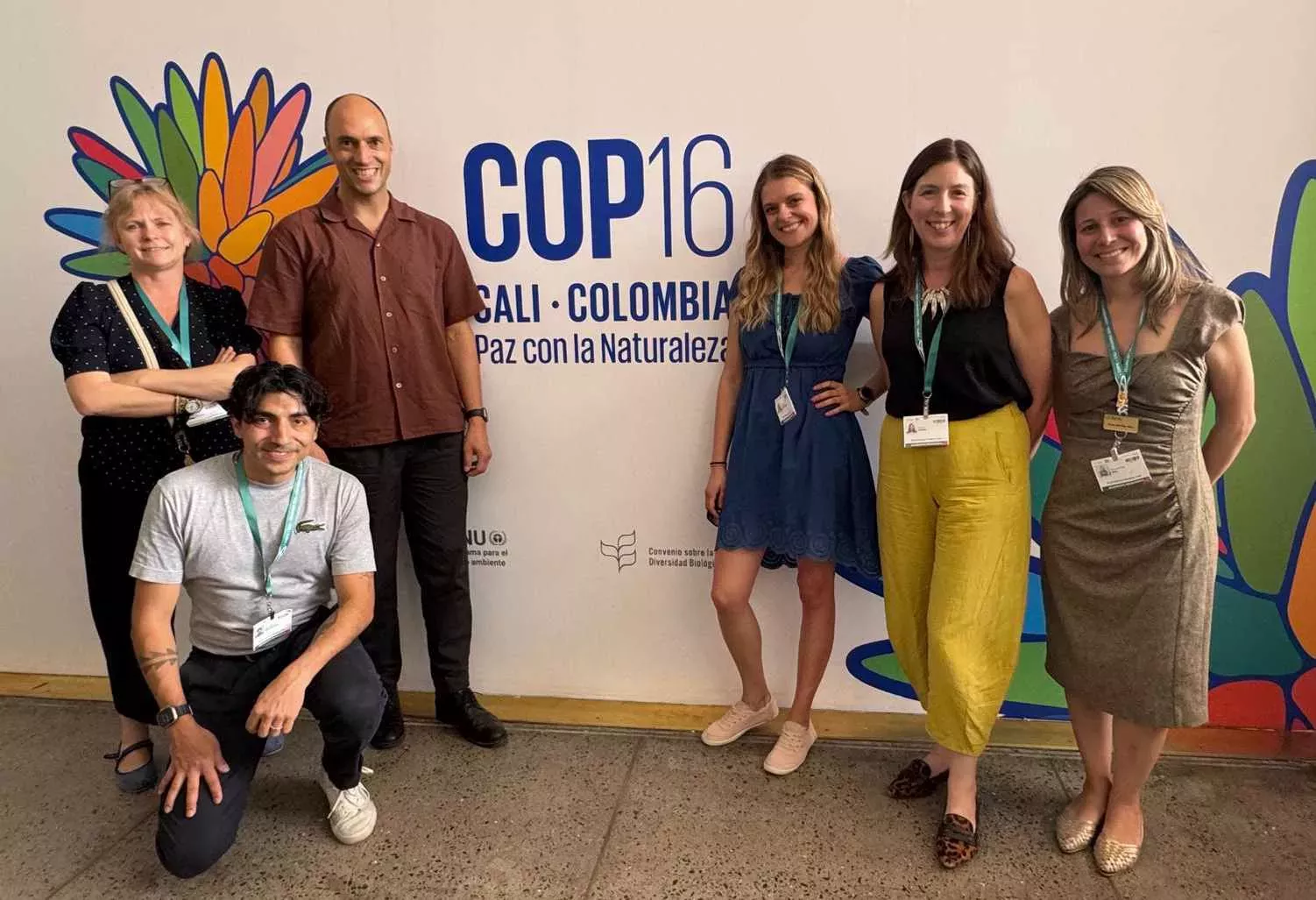 Kew representatives at COP16 in Cali, Colombia, Maria Mira © RBG Kew Six people gathered in front of a cream background reading 'COP16'